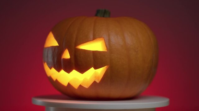 continuous looping rotation of a halloween pumpkin with carved teeth, eyes and nose, with a glowing fanar inside on a red background