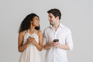 Young multiracial couple laughing while using mobile phones