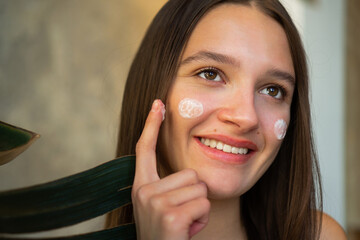 Close-up shot of a beautiful young woman applying face cream.