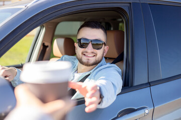 young smiling man driving car and taking away coffee.