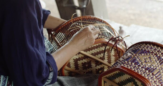Cut in shot of Thai female farmer weave basket in traditional Thai art patterns to sell as extra income in countryside of Thailand.	