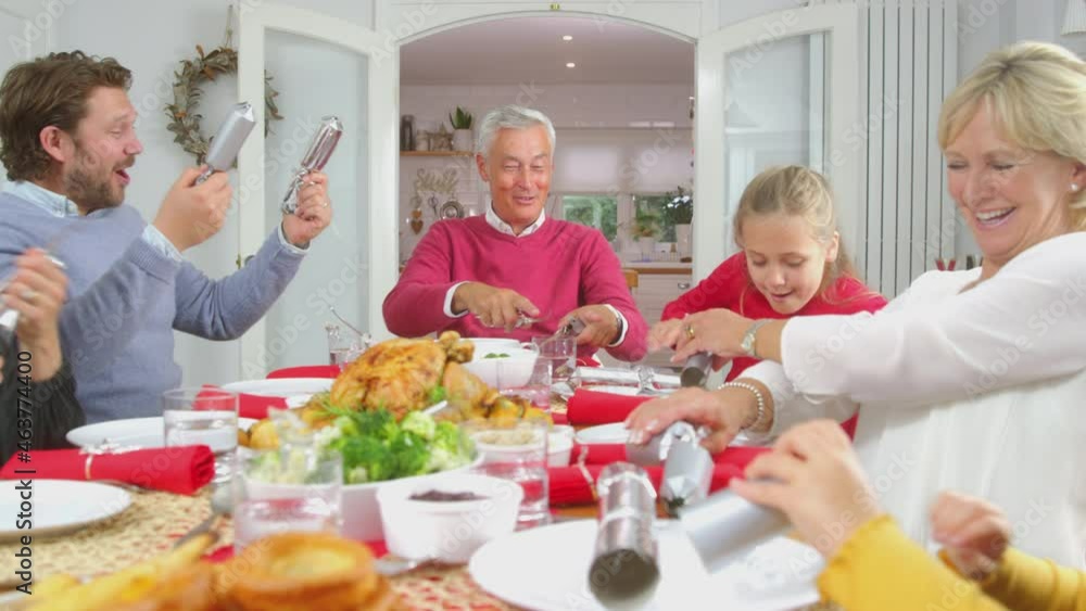 Wall mural multi generation family pulling christmas crackers before putting on paper hats and eating meal at h