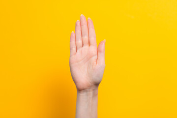 Female hand and gesture for a stop or hello. Yellow background. Close up. Copy space