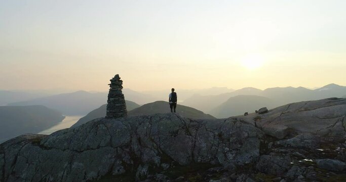 Norwegian hiker alone on mountain overlook fjord view and sunset - aerial orbit