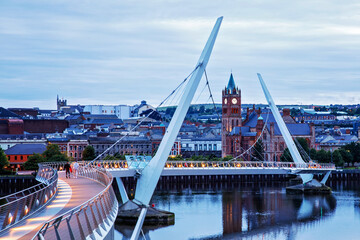 Derry, Ireland. Illuminated Peace bridge in Derry Londonderry, City of Culture, in Northern Ireland with city center at the background. Night cloudy sky with reflection in the river at the dusk