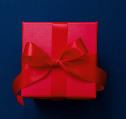 Gift box red ribbon and bow on blue background, Christmas present satin curly decoration,