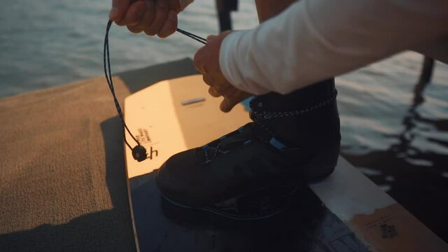 Man Tying Shoelaces on Shoes Fixed on Wakeboarding Board. Sunny Summer Day at Wakepark for Relaxation. The concept of water sports, active life