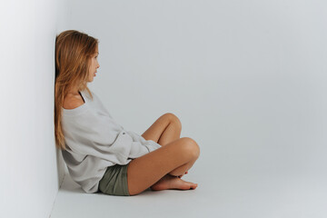 Sitting cross-legged on the floor teenage girl leaning her back against the wall