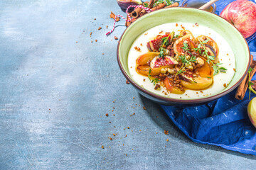 Autumn breakfast or snack, spicy semolina porridge with caramelized apples, grilled peach, plums and figs, nut, thyme, honey. Top view on blue sun lighted concrete table