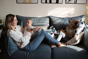 Young caucasian mother having fun on couch with two children at home during coronavirus covid-19...