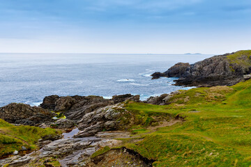 Rugged landscape at Malin Head, County Donegal, Ireland. Rough beach with cliffs, green rocky land with sheep on foggy cloudy day.