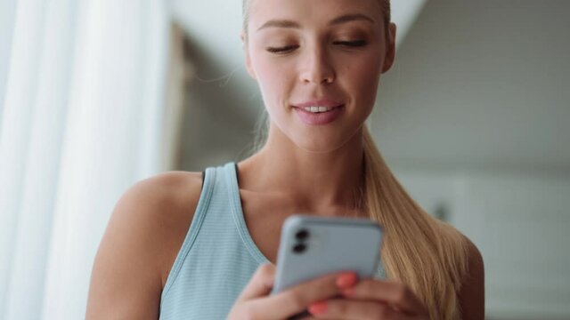 Positive Blond Woman Texting By Phone And Looking To The Side At Home