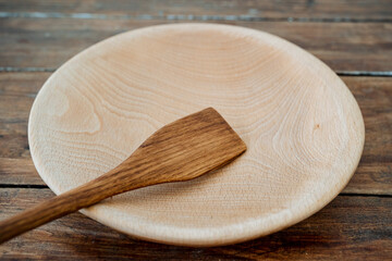 Kitchen utensils made of quality materials. A close shot of a wooden round plate and a spatula. A set of appliances in the kitchen made of wood