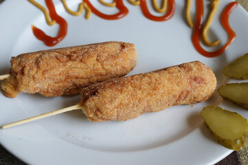 home made corn dogs on a white plate. corn dogs with ketchup and mustard
