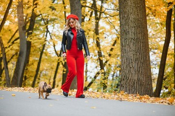 Fototapeta premium a stylish young girl with long light hair in sunny glasses goes for a walk with a little middle doggy a pug by the French bulldog in a park in spring in autumn