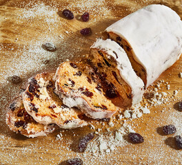 A Christmas stollen lies on a board sprinkled with powder and raisins. 