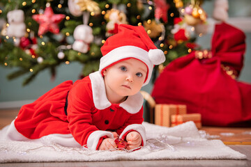 An adorable kid dressed as Santa Claus plays near a decorated Christmas tree in the living room.