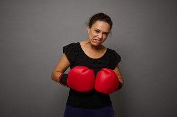 Strong African woman poses against gray wall background with red boxing gloves. Concept of Black Friday and boxing Day, Blow to prices with copy space for advertisement