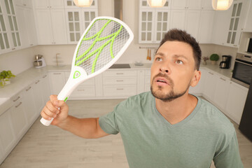 Man with electric fly swatter in kitchen. Insect killer