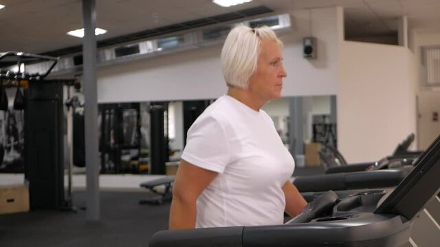 elderly woman with gray hair plays sports in gym. Active healthy lifestyle, pensioner, senior concept. Rehabilitation after injuries, strengthening immunity, losing weight, improving well-being.