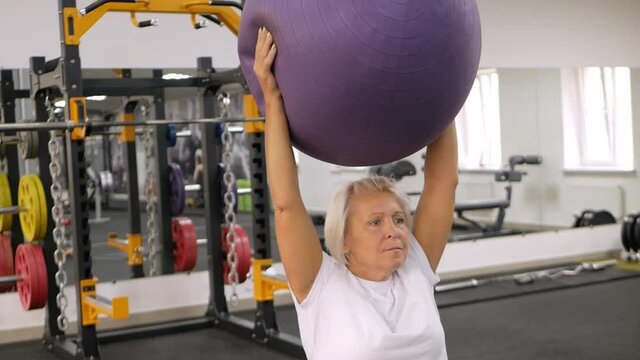 elderly woman with gray hair plays sports in gym. Active healthy lifestyle, pensioner, senior concept. Rehabilitation after injuries, strengthening immunity, losing weight, gymnastic ball