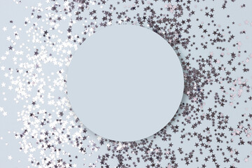 Round frame made of silver colored stars confetti on a blue pastel background.