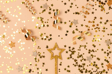 Glittering magic wand with gold colored confetti on a beige background.