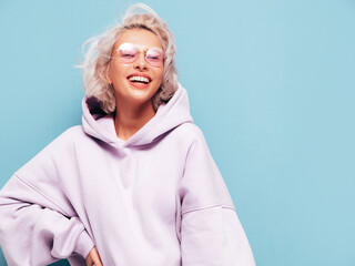 Young beautiful smiling female in trendy summer hoodie. Sexy carefree woman posing near blue wall...