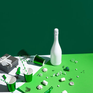 Christmas composition made of paper glasses with straws, present box, white champagne bottle, meringues and green baubles. Festive and party concept. 2022 new year background.