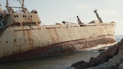 Old rusty boat left after crash on seaside. Wrecked fishing ship on water. Sunny weather outdoors.