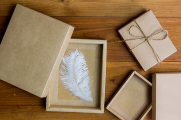 Craft gift box with white feather on wooden table. 