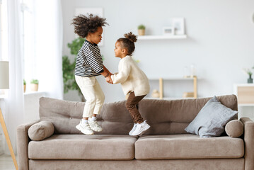 Happy energetic african american children jumping on sofa - Powered by Adobe