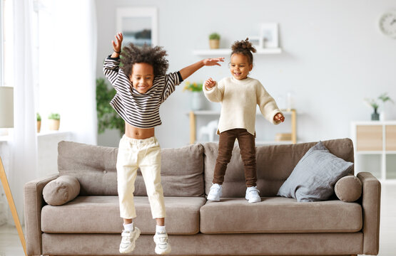 Happy energetic african american children jumping on sofa