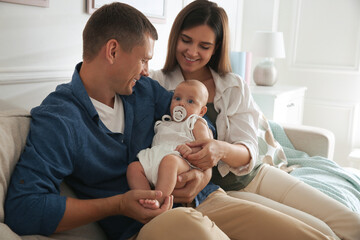 Happy couple holding their cute little baby with pacifier at home