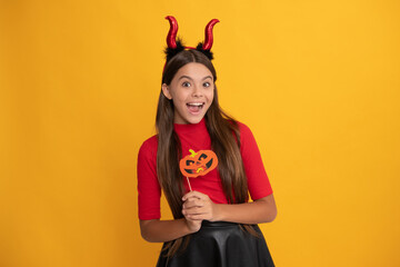 glad teen girl wearing imp horns holding pumpkin party accessory, happy halloween.