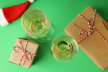 Glasses of champagne, Santa hat and gift boxes on green background