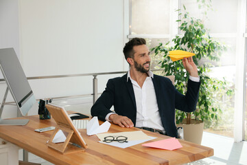 Handsome businessman playing with paper plane at desk in office