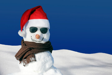 Happy snowman with red Santa Claus hat, sunglasses, winter landscape, white snow, blue sky.