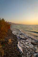 Amazing colors of sunrise over a wild and natural beach in the Dead Sea With a green plastic bottle thrown on the beach, against the backdrop of Mountains