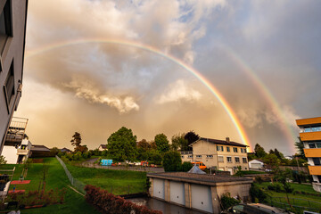 Beautiful double rainbow with European houses and cloudy sky in Cossonay, Switzerland