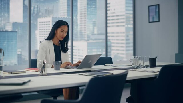 Portrait of Successful Asian Businesswoman Wearing in Stylish Suit Working on Laptop Computer in Big City Office. Female Executive Director Managing Digital e-Commerce Project, Data Analysis