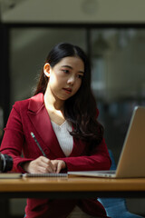 Focused young businesswoman using laptop computer and doing some paperwork