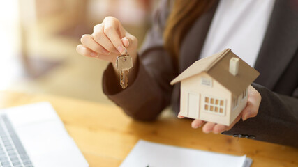 Female house insurance broker or real estate agent holding house key and house model