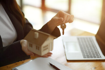 Female realtor broker holding home keychain and house model in her hand