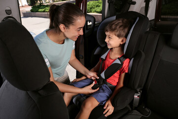 Mother fastening her son with car safety belt in child seat