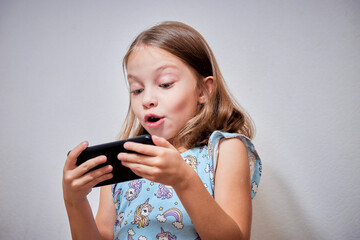 a little preschool girl plays online games on her smartphone and watches cartoons