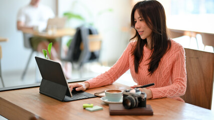 Attractive asian young female freelancer working on portable tablet computer at a cozy cafe.