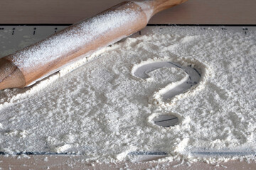 Question mark on the background of flour. What to cook dinner? Concept question  home baking. Question mark drawn on scattered flour on table with wooden rolling pin.
