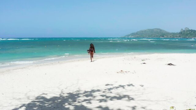 Young brunette girl in bikini explores Playa Teco Maimon near Puerto Plata Dominican Republic, drone slide left