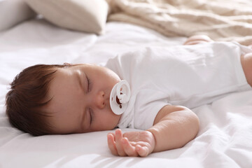 Cute little baby with pacifier sleeping on bed